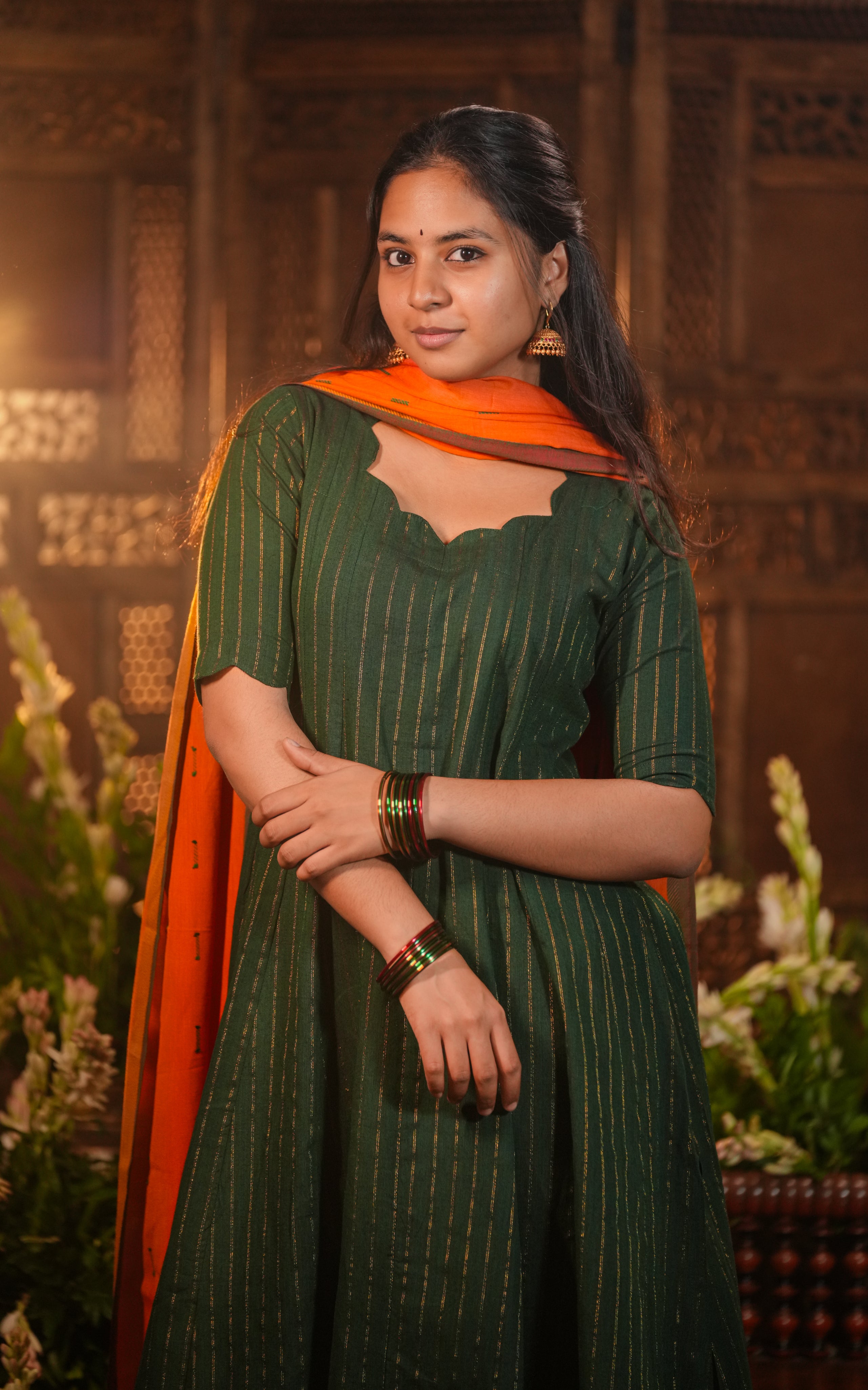 Woman wearing a deep green Anarkali with vertical golden threadwork.