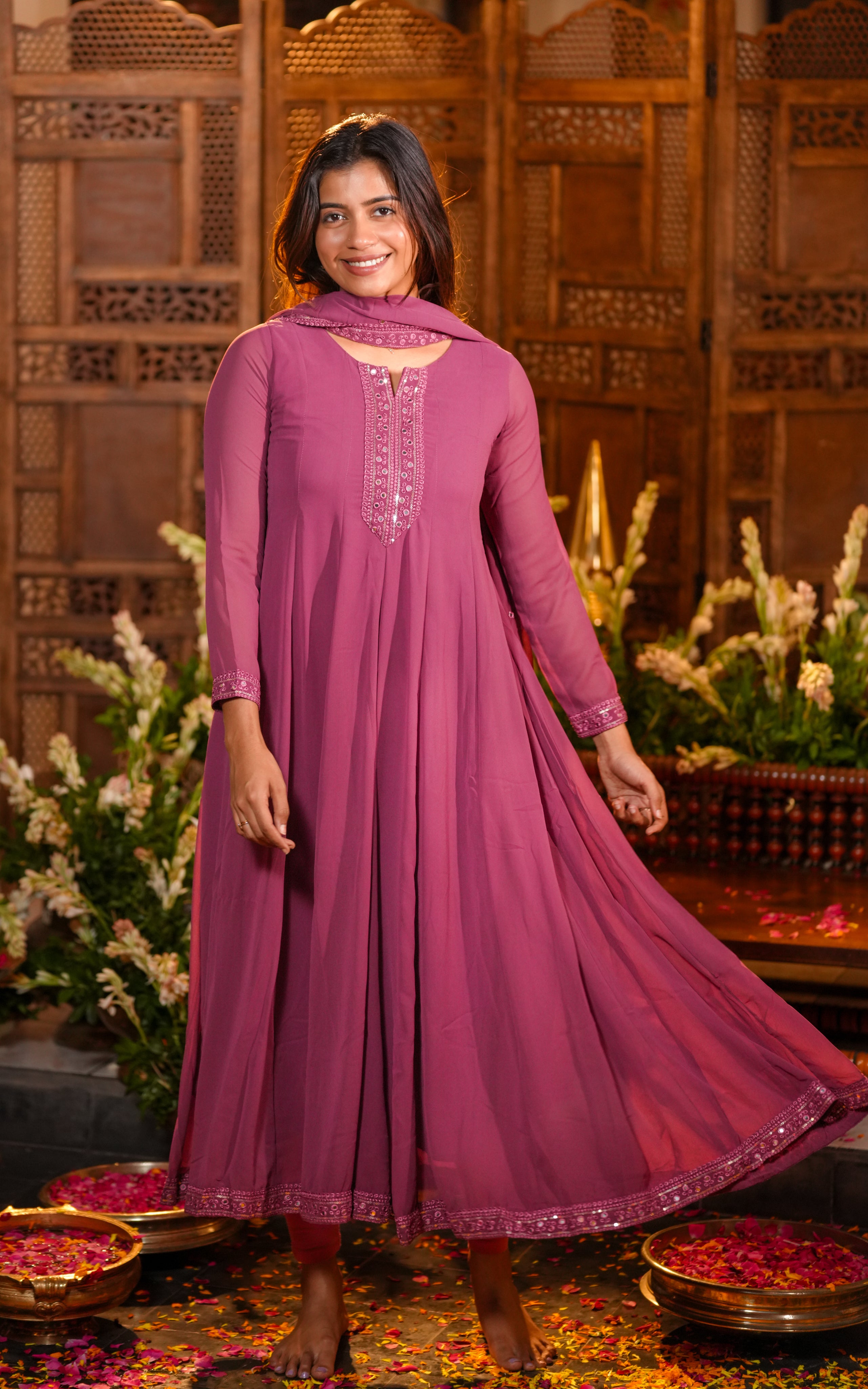 A woman is wearing an onion pink Anarkali dress made from lightweight georgette fabric.