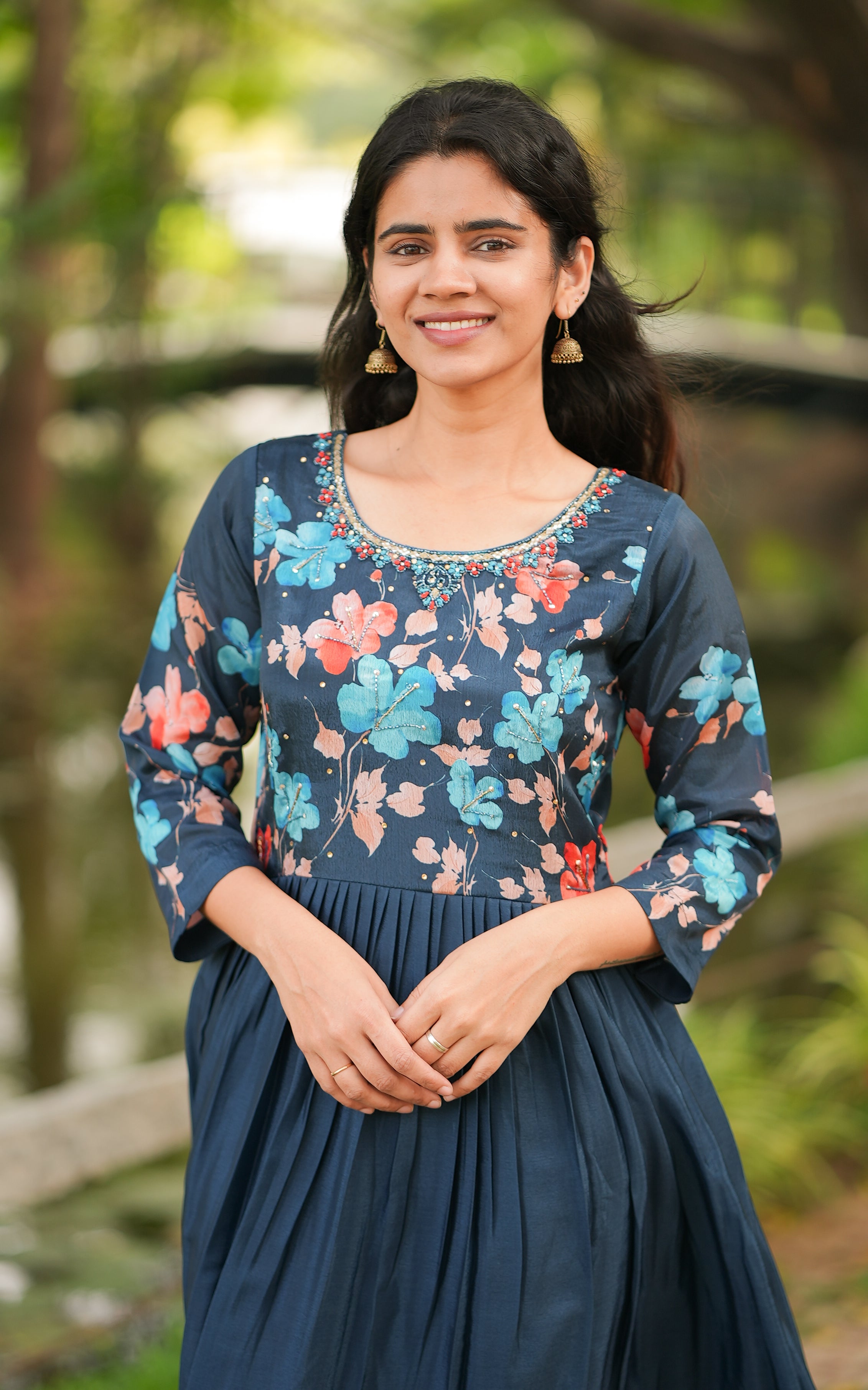 A woman wearing a blue full flared anarkali dress with floral print and long sleeves, standing outdoors.