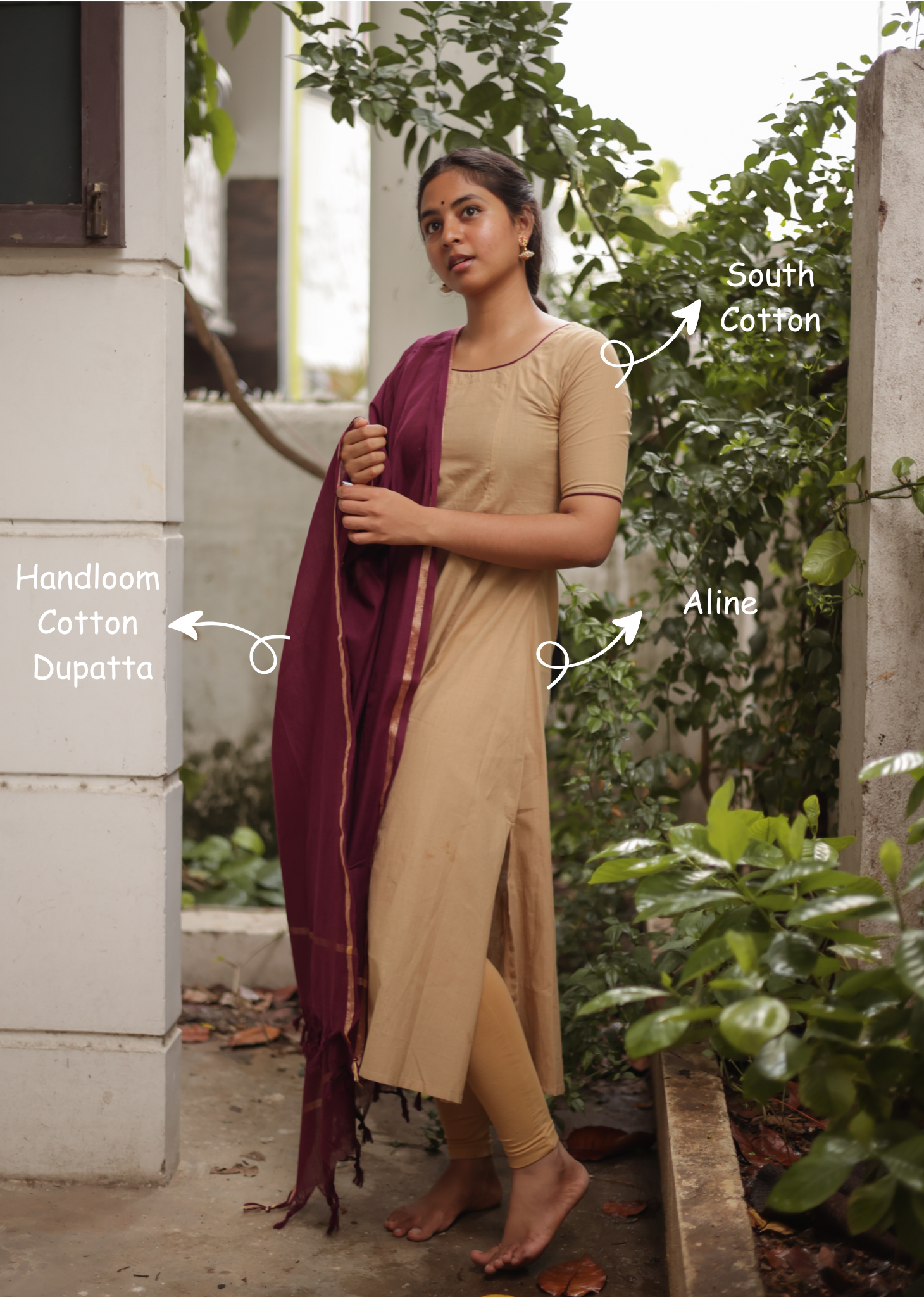 Woman wearing a beige saree with a purple dupatta, standing outdoors with greenery in the background.