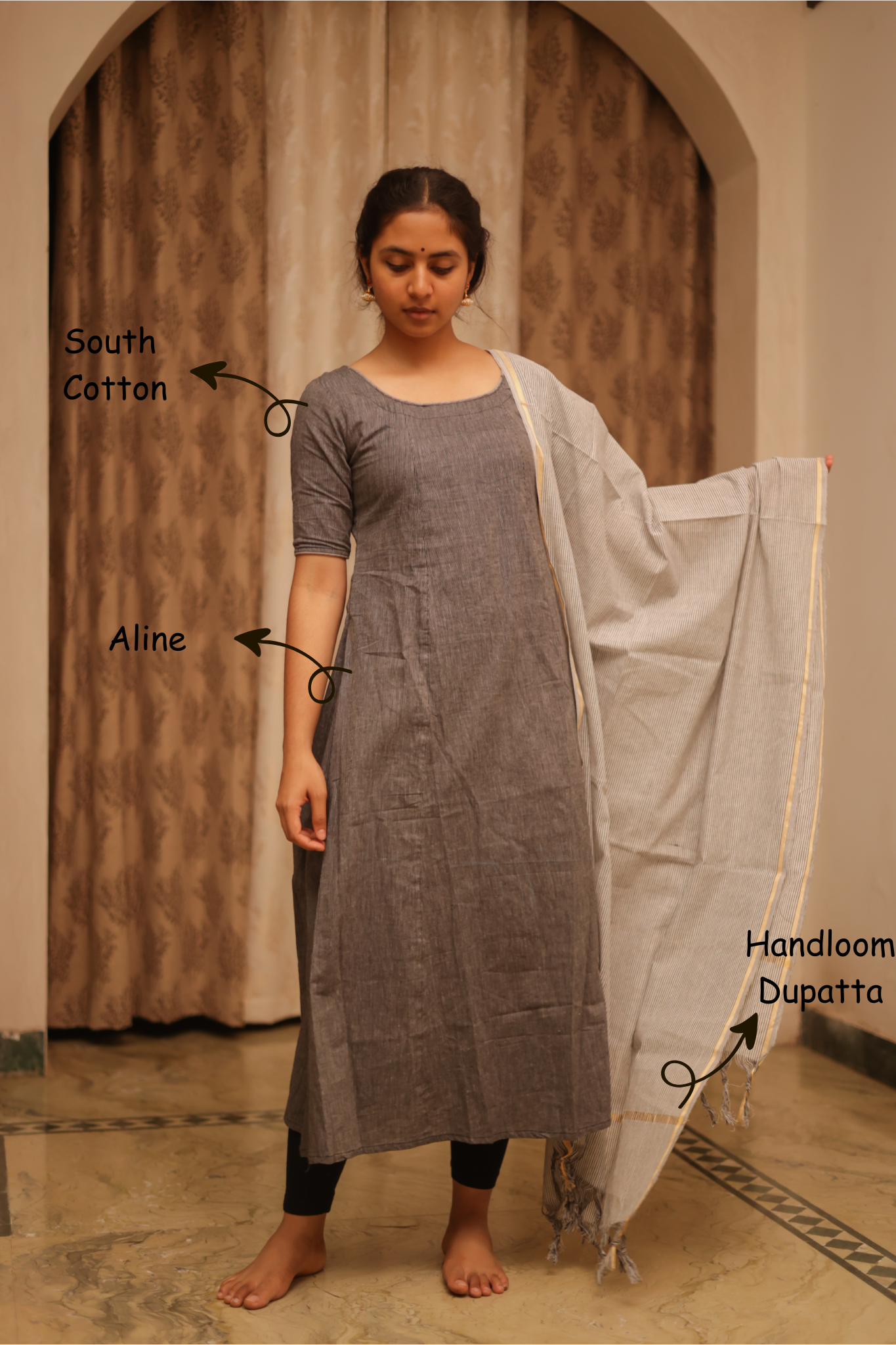 Woman wearing a gray kurta with a white dupatta, standing indoors.