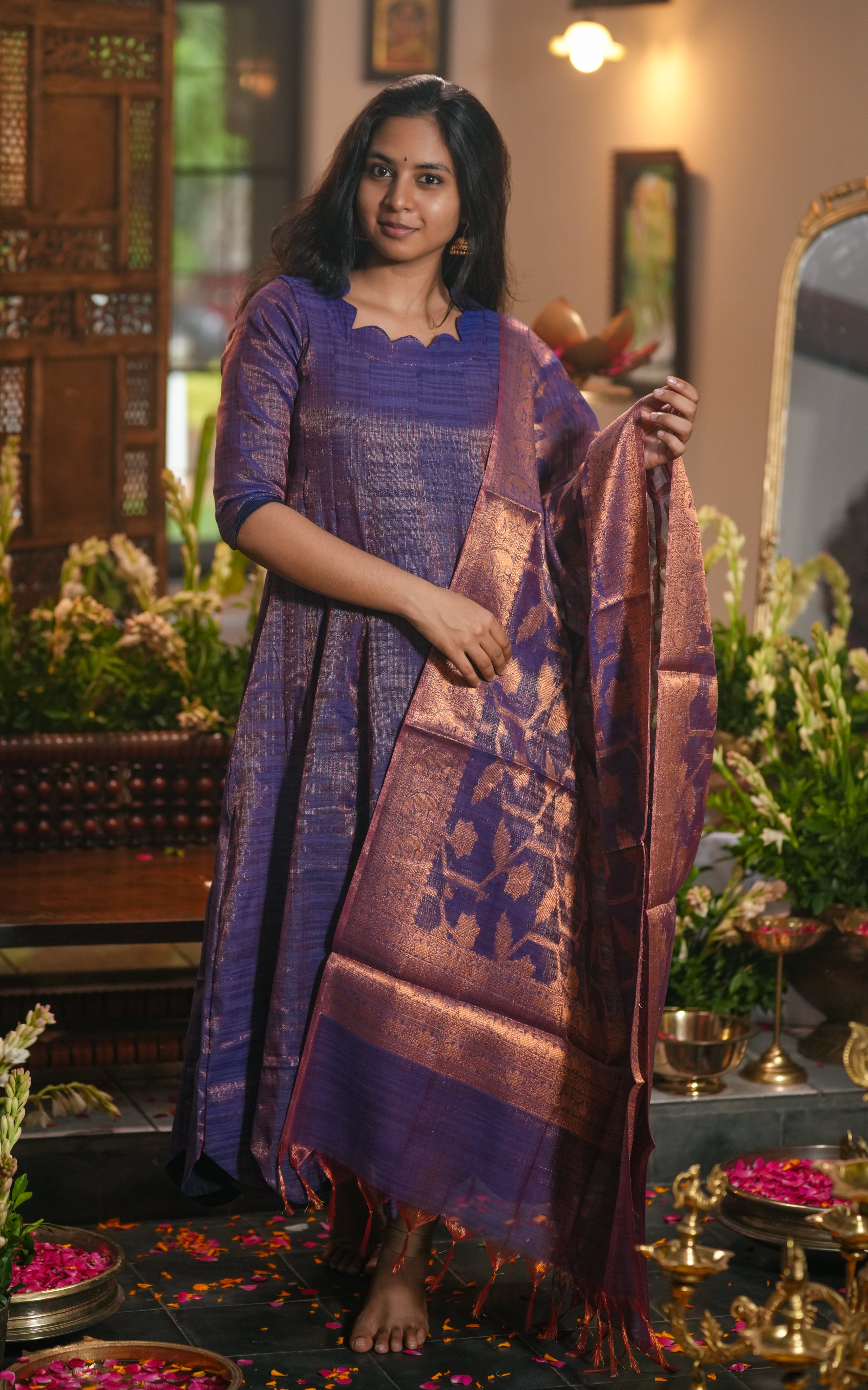 Woman wearing a violet silk Anarkali with a scalloped neckline and matching zari dupatta.