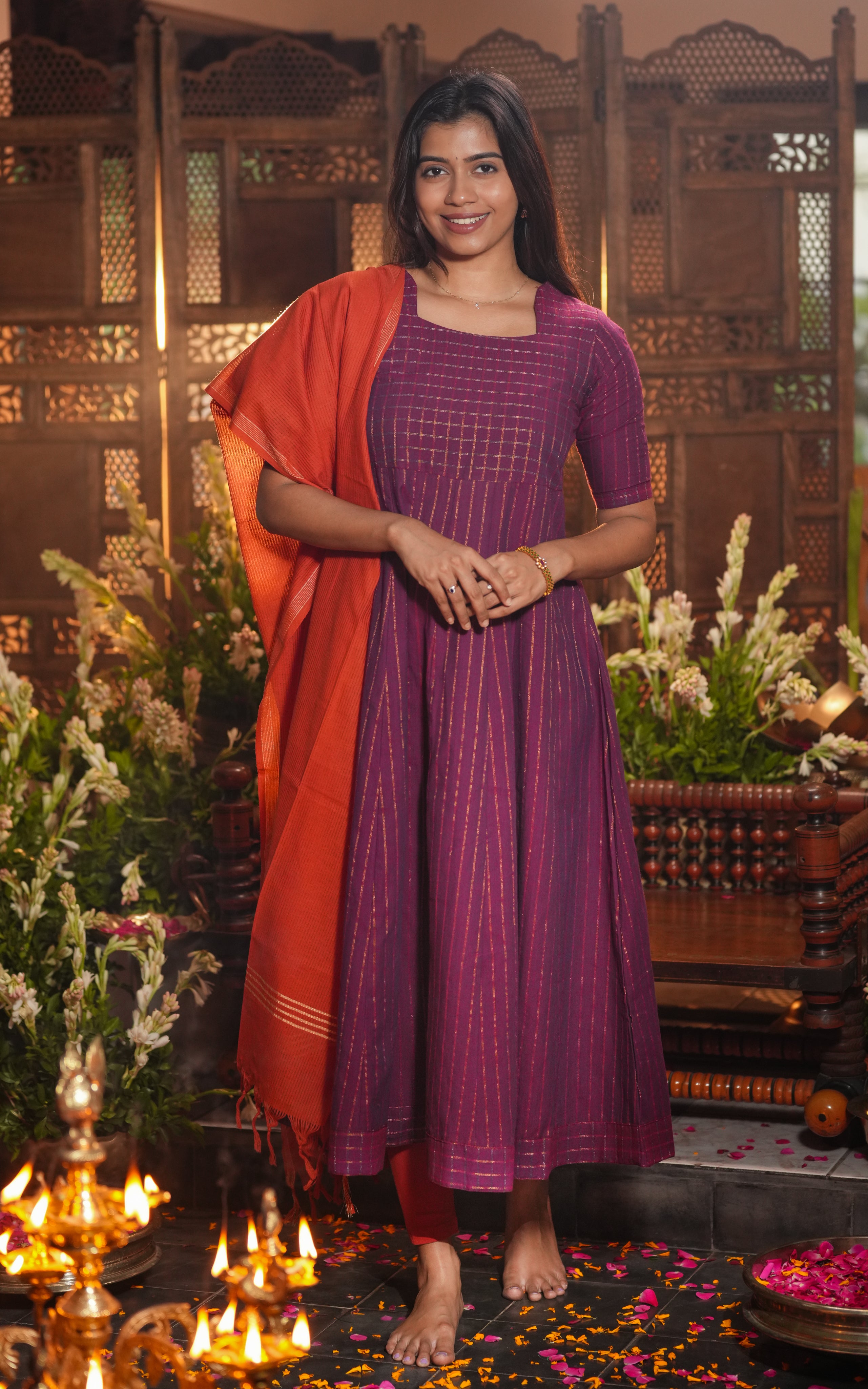 Woman dressed in a purple Anarkali with golden stripes, styled with a brick red cotton dupatta.