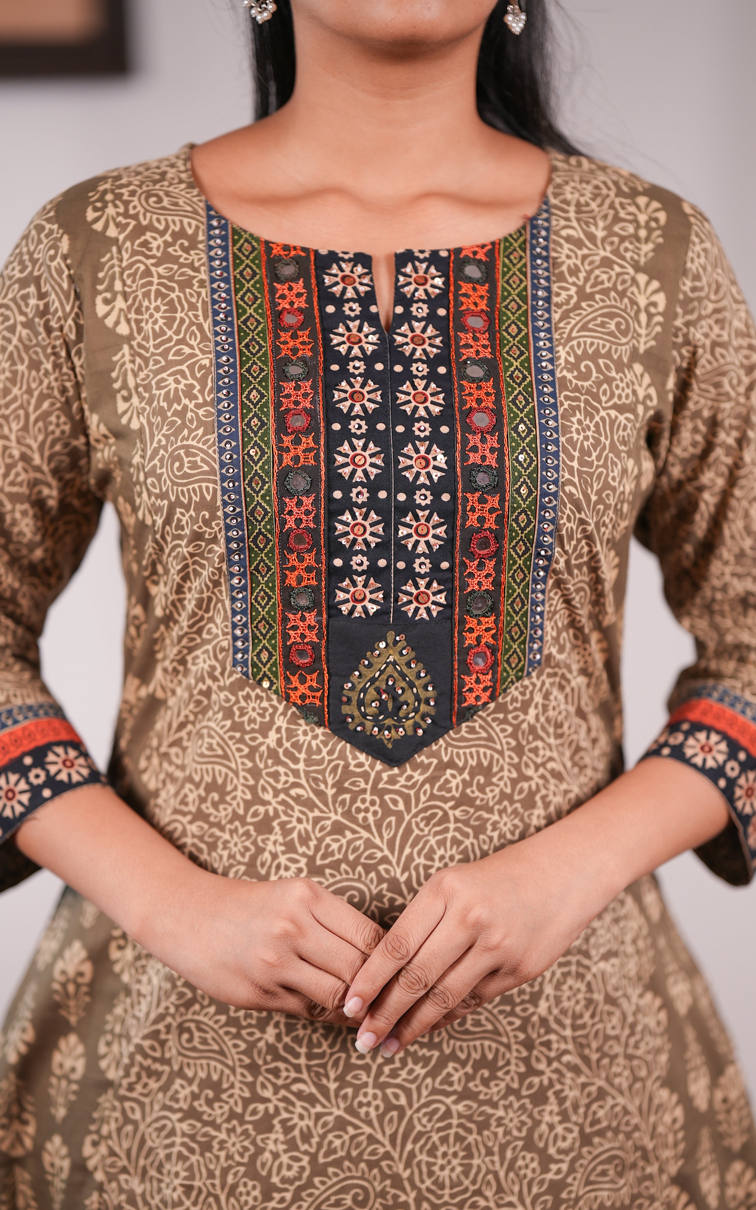 Brown patterned dress with intricate neckline design on a blurred background