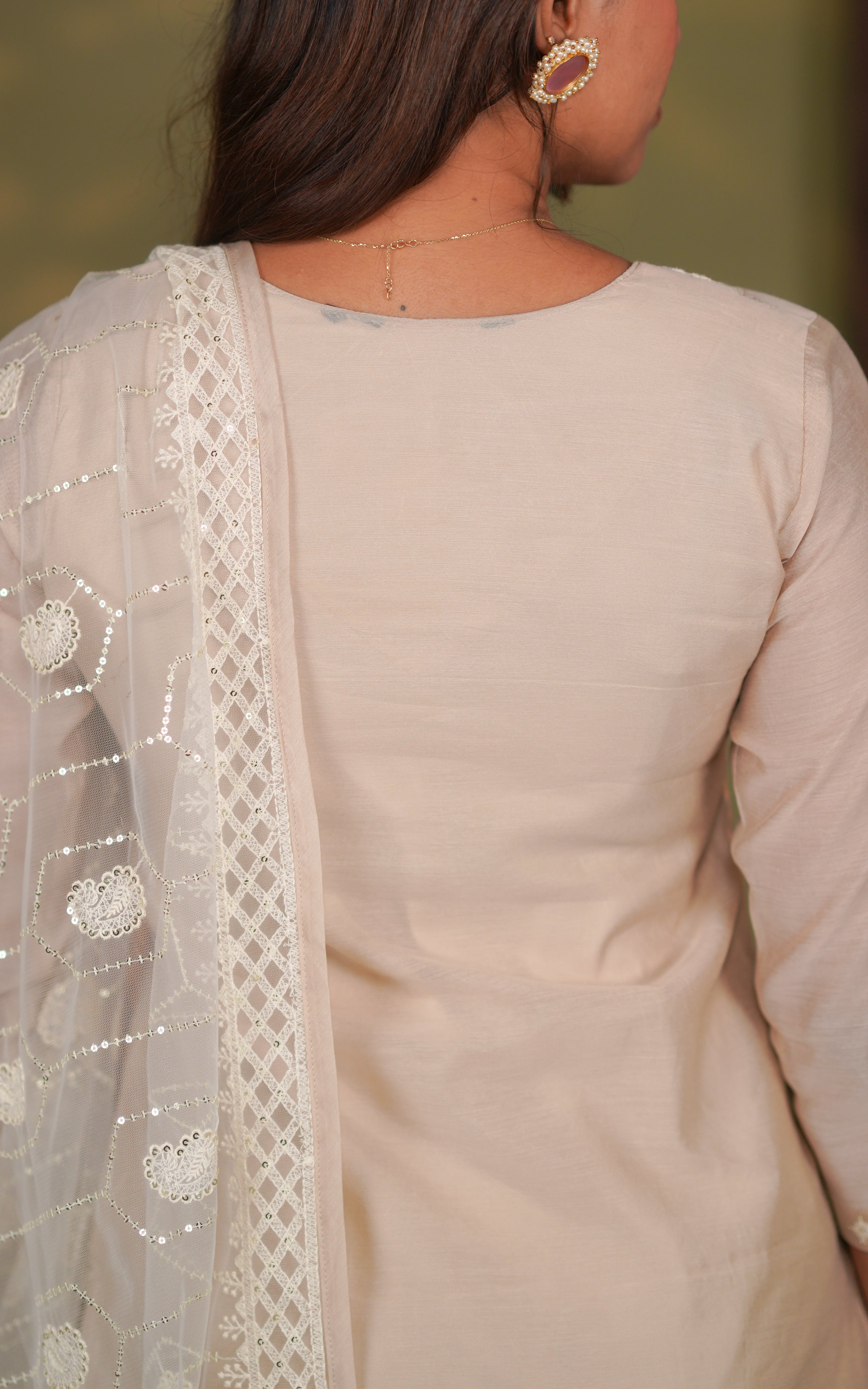 Woman wearing a light-colored traditional outfit with a sheer dupatta.